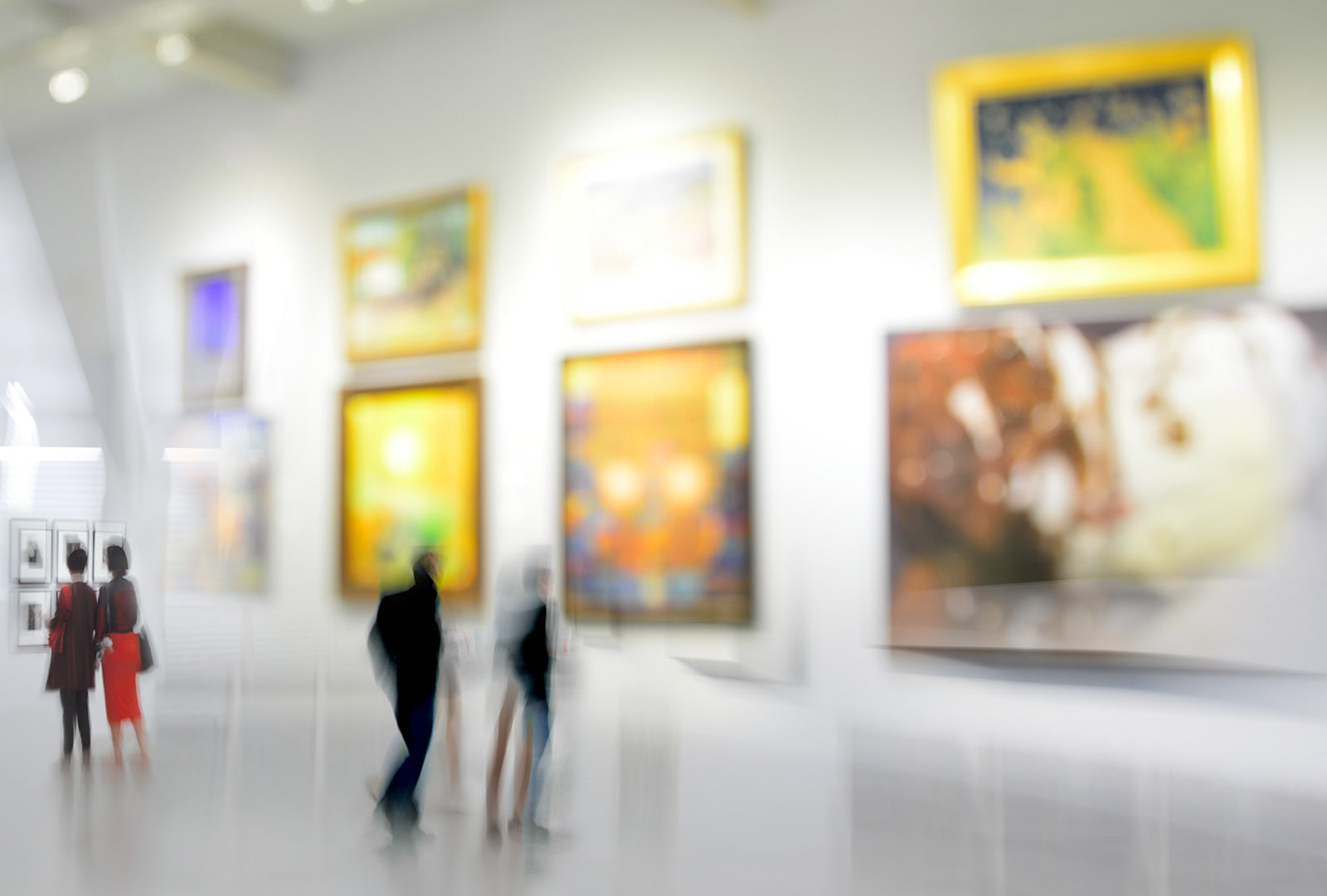 Blurred image of people in an art gallery with colorful paintings on the wall.