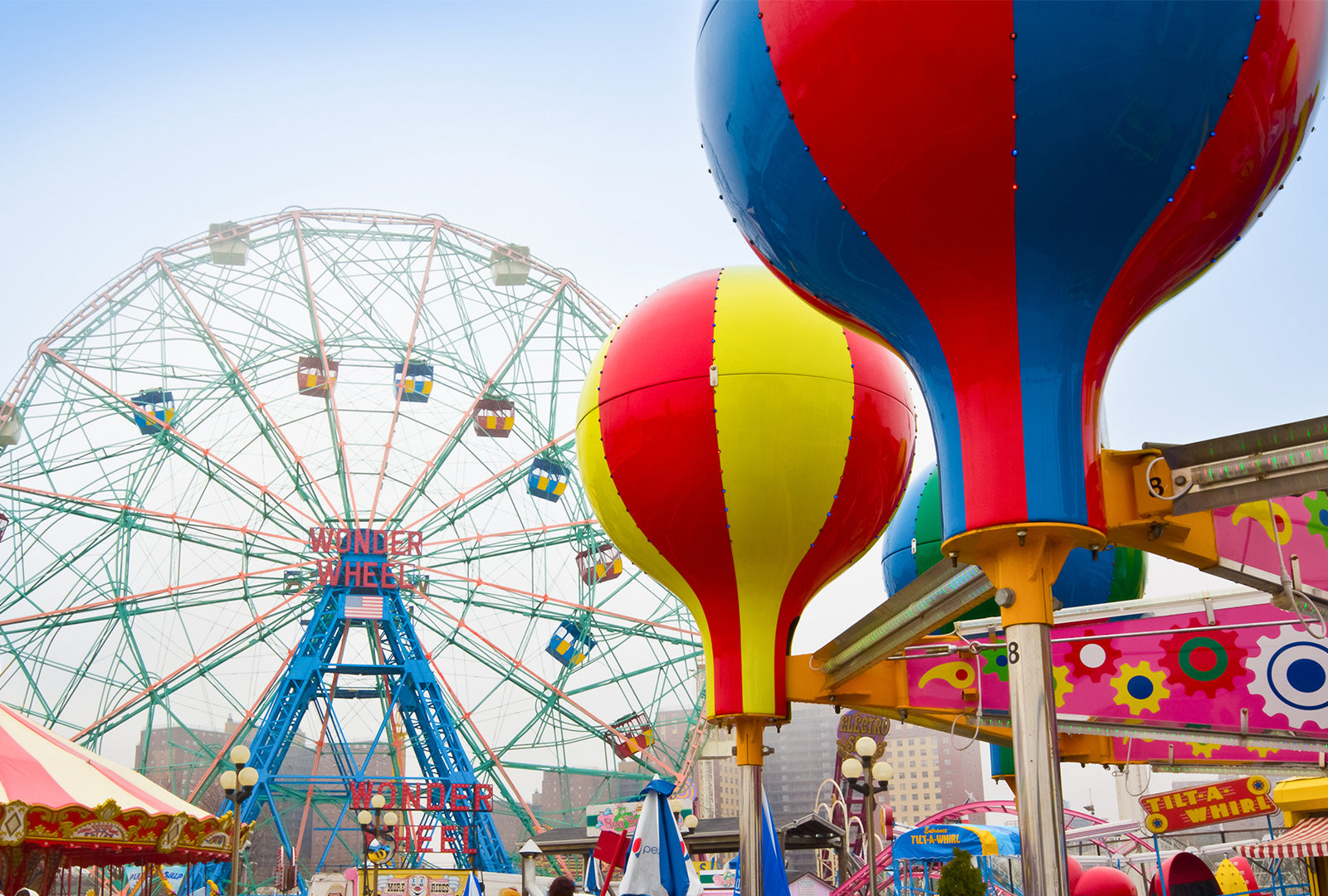 Colorful carnival scene with Ferris wheel and hot air balloons against a blue sky.