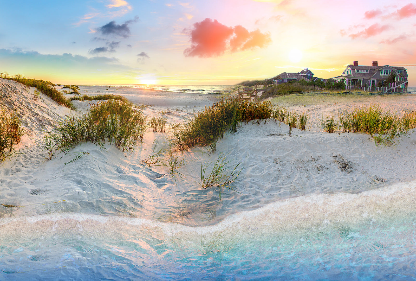 Sunset over a beach with sand dunes and houses in the background