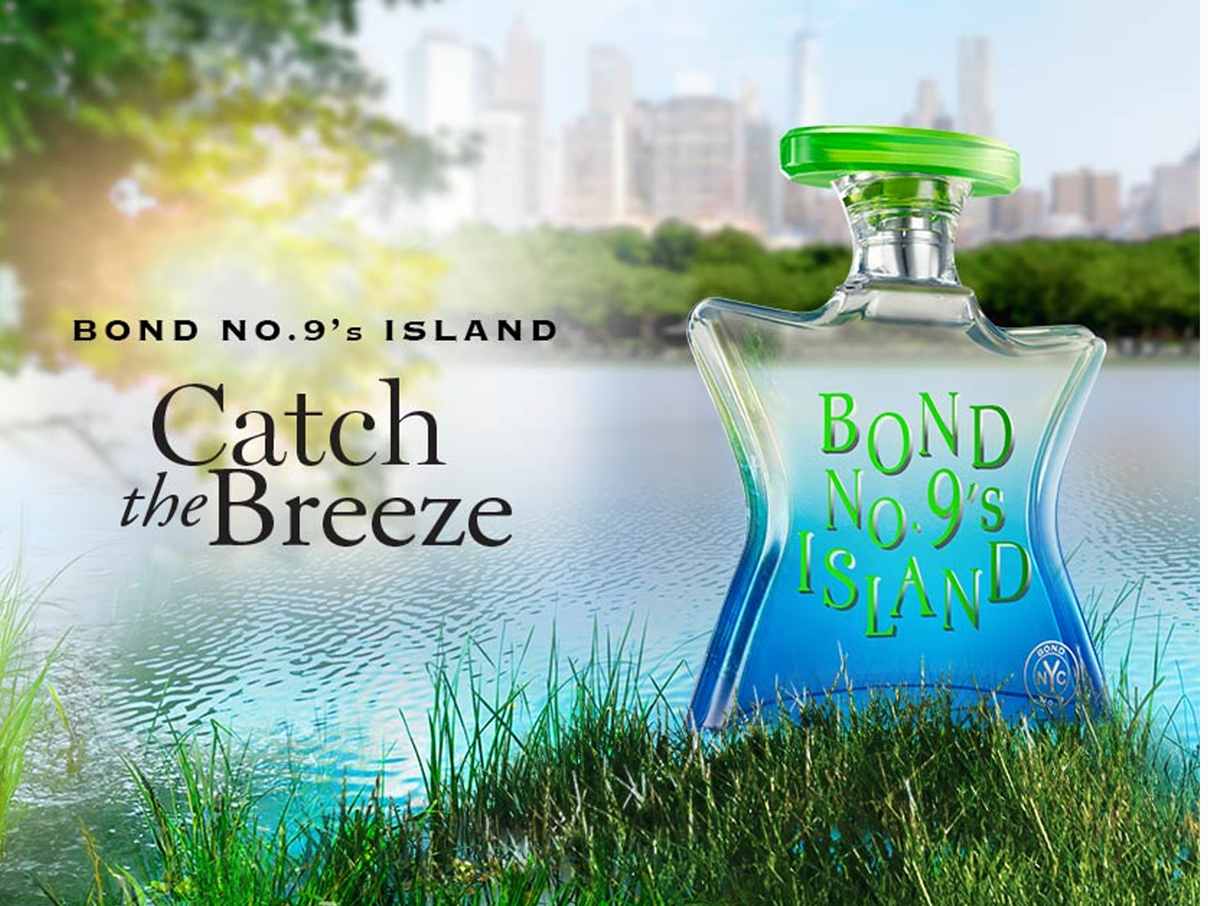 Bond No. 9's Island 'Catch the Breeze fragrance bottle placed on grass by a lake, with a blurred city skyline and trees in the background.