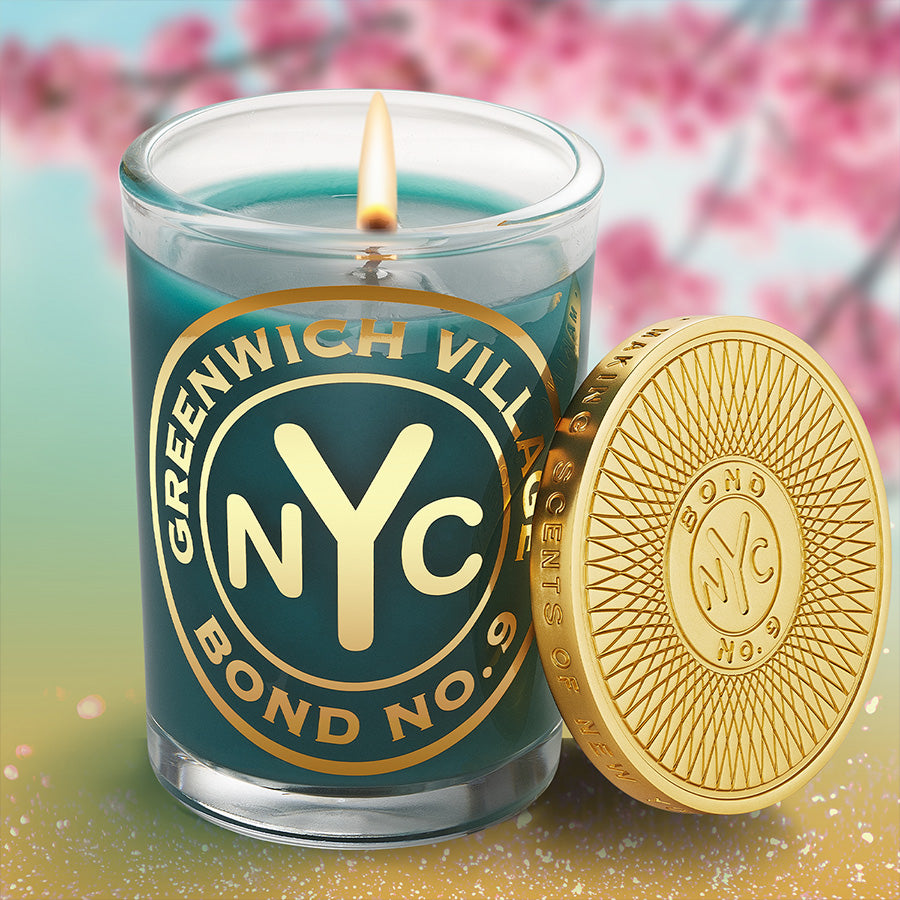 Candle with 'Greenwich Village NYC' branding and a gold coin on a colorful background